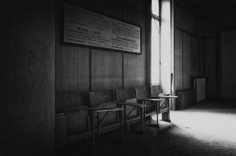 Row of chairs beneath a wall notice in a dark room, in black and white.