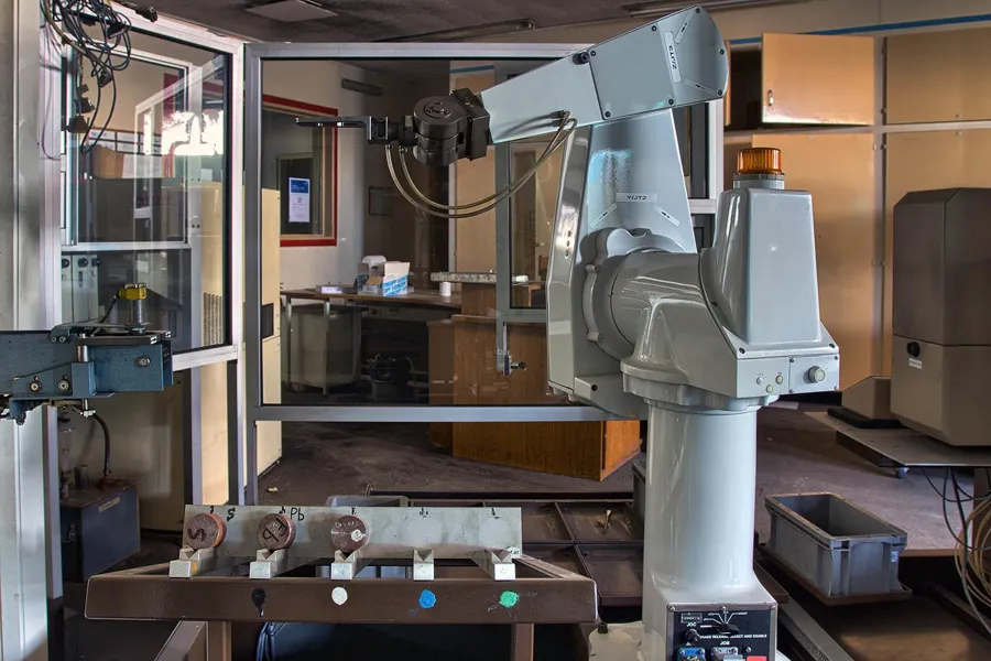 Grote grijze robotarm naast een afgesloten werkruimte.