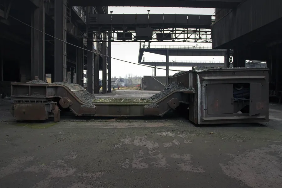 Empty dark hall with heavy metal structures near a large opening.