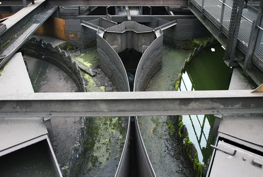 Curved concrete channels with green residual water seen from above.