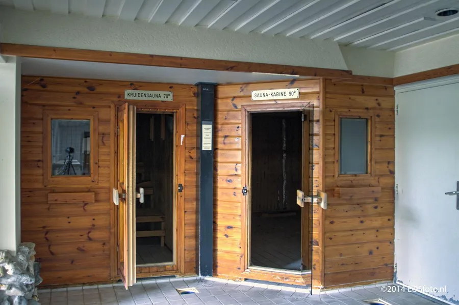 Dos puertas de sauna abiertas en una pared de madera con rótulos.