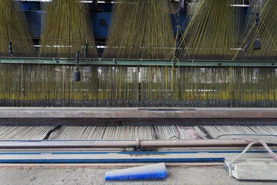 Máquina textil con muchos hilos colgantes y un cepillo azul delante.