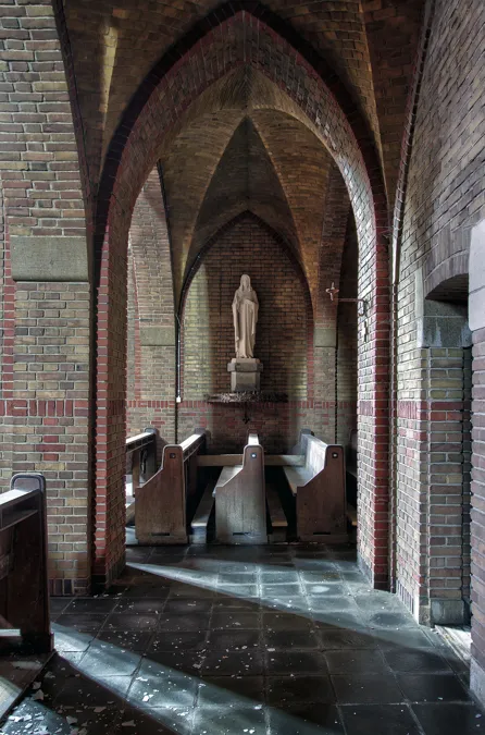 Schmaler Seitenraum unter Spitzbögen mit Bänken und Figur am Ende.