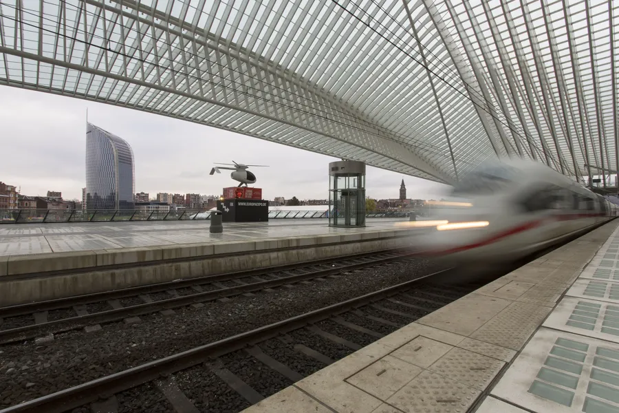 Tren blanco en movimiento desenfocado bajo la cubierta, con borde del andén y nervaduras nítidos.