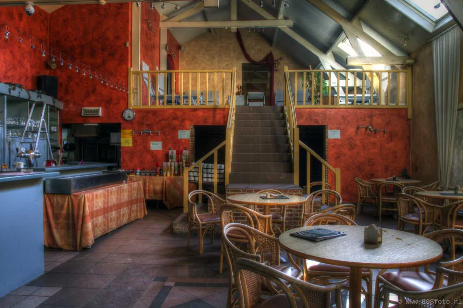 Leerer Sitzbereich mit Korbstühlen, Bar und Treppe vor roter Wand.