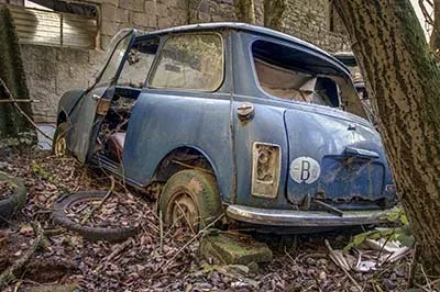 Rear of a rusty blue Mini with missing tail light and flat tyre.