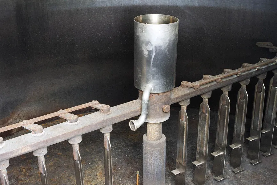 Metalltrichter mit kleinem Hahn über schmalen Haltern an einer alten Maschine.