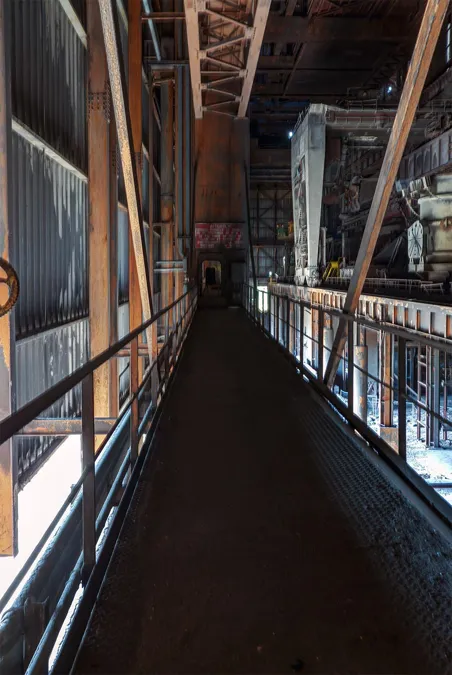 Smalle metalen loopbrug langs de zijwand van een hoge fabriekshal.