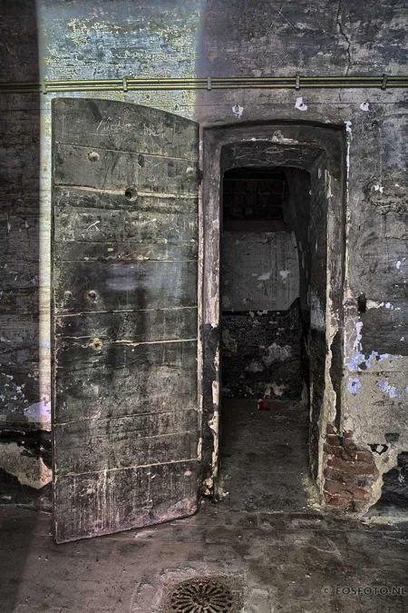 Heavy open wooden cell door in a damaged wall.