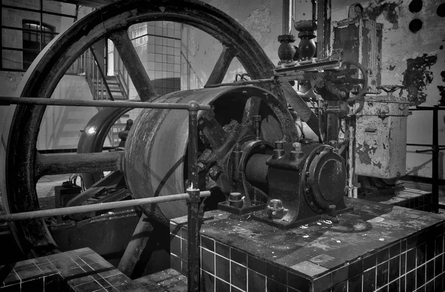 Schwarz-Weiß-Detail eines großen Schwungrads und der damit verbundenen Industriemaschine.