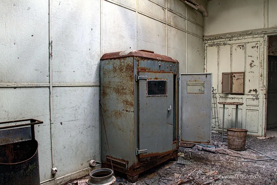 Armoire métallique rouillée à porte ouverte dans une pièce dégradée.