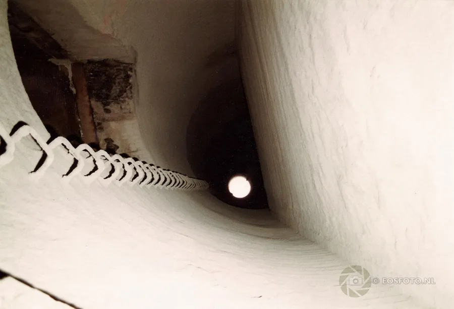 Interior de una chimenea alta con escalera hacia una abertura circular de luz.