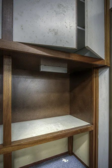Oude houten werkhoek met plank, metalen bovenkast en een verlichtingsbalk.