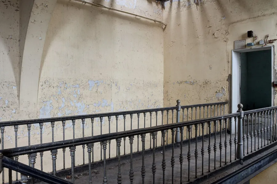 Langes Metallgeländer an abblätternder Wand vor grüner Tür.