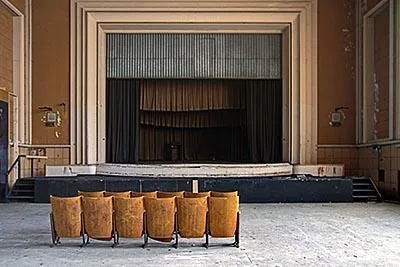 Row of yellow theatre seats facing a stage with layered curtains.