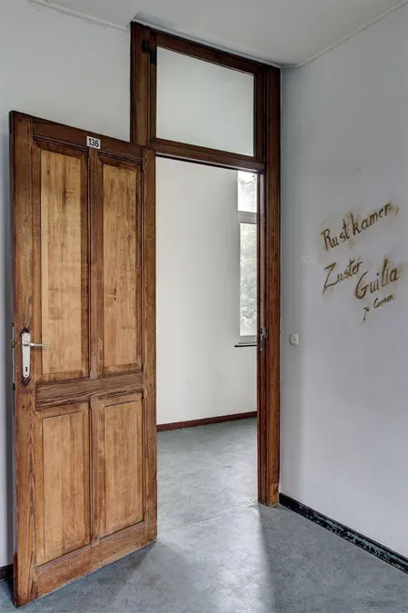 Puerta de madera abierta junto a letras manuscritas en pared blanca.