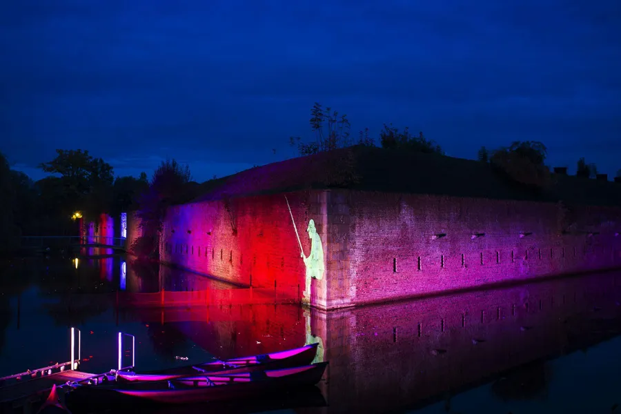 Roodpaarse vestingmuur weerspiegelt in water onder een diepblauwe avondlucht.