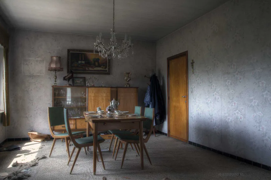 Esstisch mit Stühlen unter einem Kronleuchter in kahlem Zimmer.