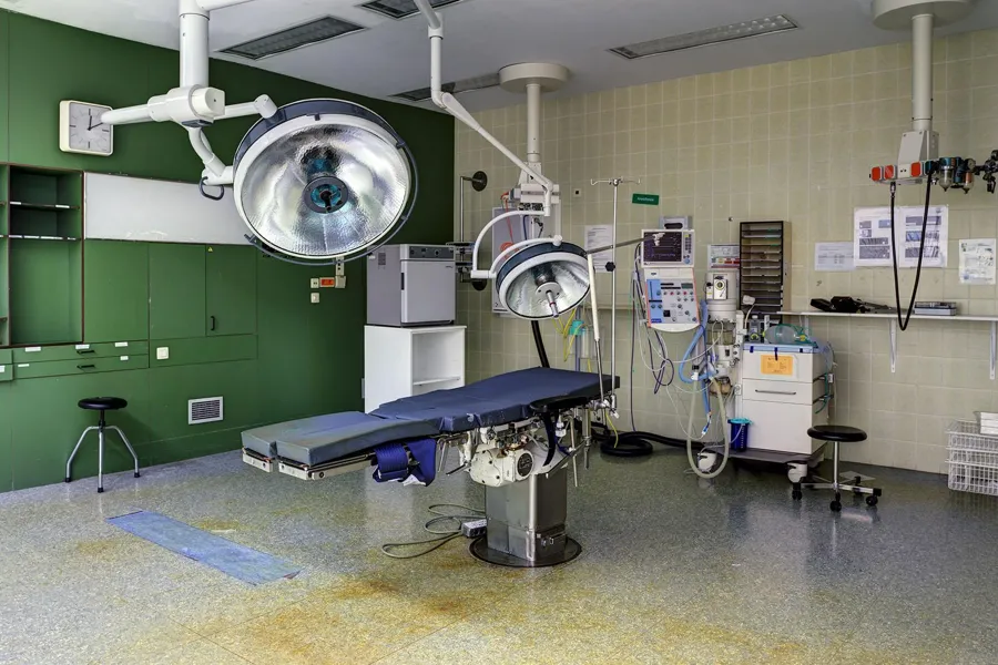 Blue operating table beneath two lights in a green operating room.