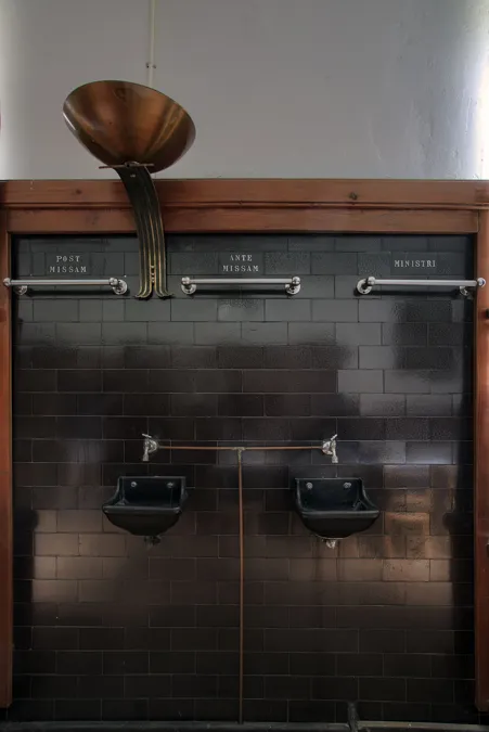 Panel de madera con dos timbres negros y tubo acústico de metal encima.