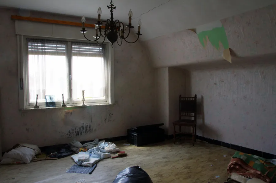 Kronleuchter und Holzstuhl in einem fast leeren Zimmer.