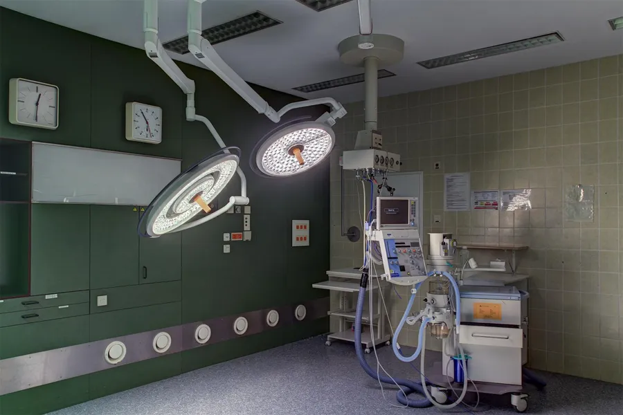 Two illuminated surgical lights beside equipment and a green wall.