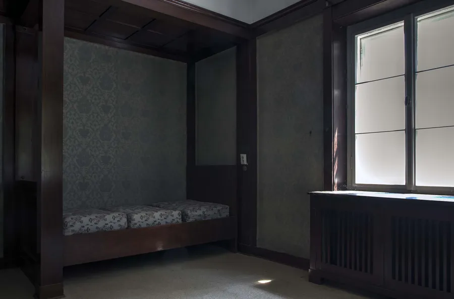Houten bed onder een nis naast een raam en radiator