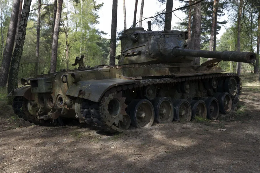 Seitenansicht eines Panzers mit langem Rohr und Laufrollen im lichten Wald.