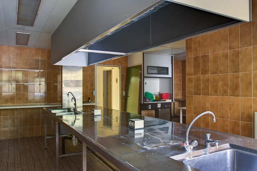 Long stainless steel worktable with sinks beneath an extractor hood.