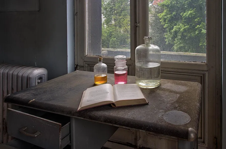 Open book and three glass bottles on a table beside the window.