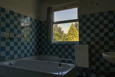 Bañera bajo una ventana entre azulejos azules y blancos.