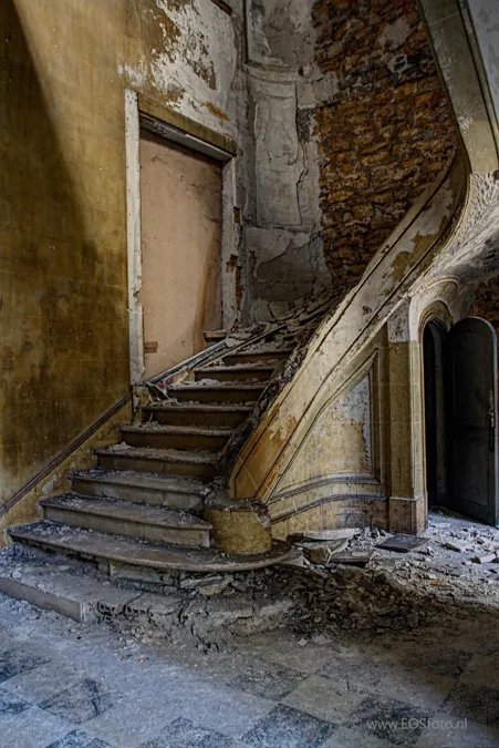 Escalier courbe abîmé entre des murs qui s’effritent.