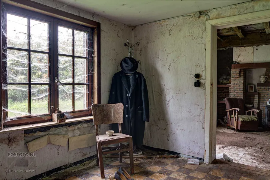 Manteau et chapeau au mur près d'une fenêtre et d'une chaise en bois