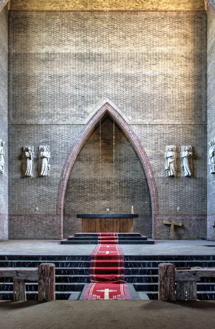Roter Läufer zwischen Bänken zum Altar unter hoher Spitzbogennische.