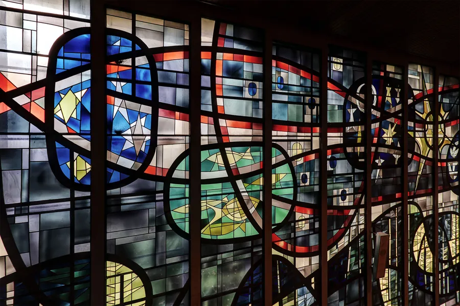 Detail of abstract stained glass with black lines, red bands and blue figures.