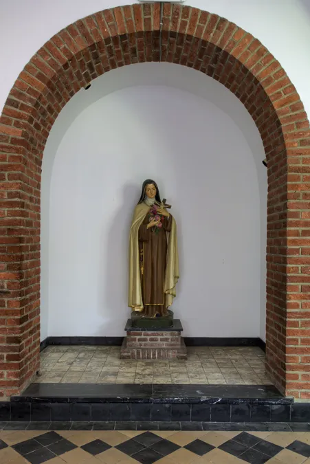 Estatua de un santo en un nicho blanco con arco de ladrillo.