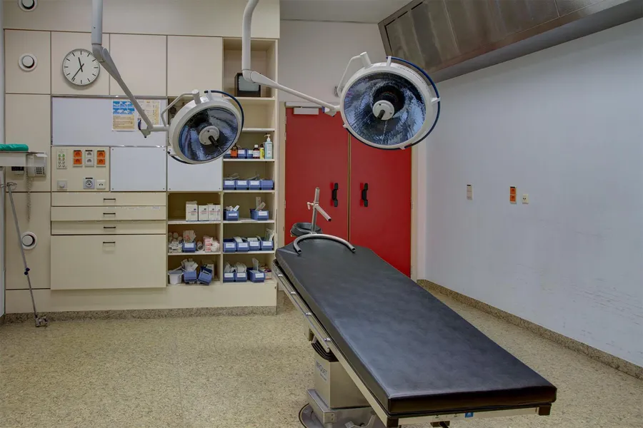 Operating table beneath two round lights beside red double doors.