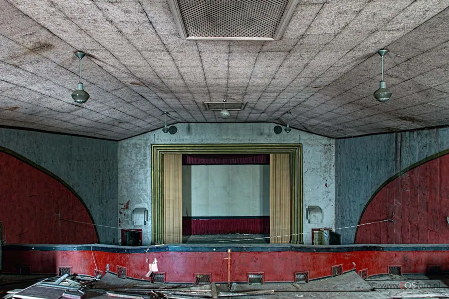Empty cinema auditorium with red semicircular wall panels and a screen at the end.