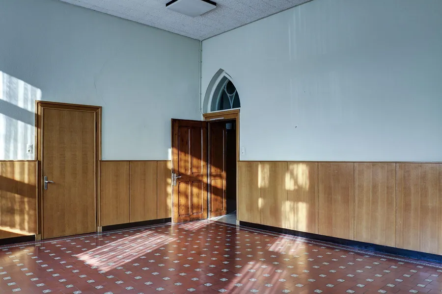 Lege lichtblauwe kamer met houten lambrisering en zonlicht op de tegelvloer.