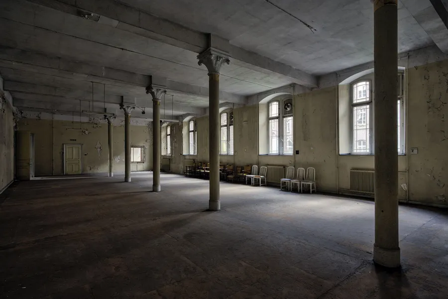 Sala grande con columnas redondas, techo plano y bancos junto a la pared.