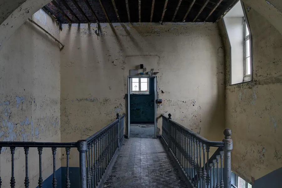 Treppenabsatz über Treppenhaus mit offenen Deckenbalken und zwei hohen Fenstern.