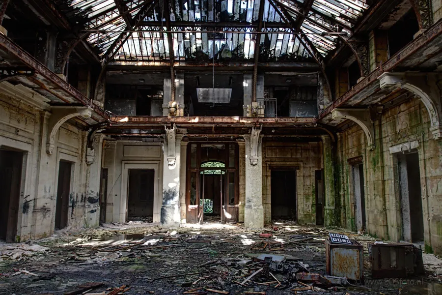 Grand hall aux portes ouvertes, aux gravats et à la verrière cassée.