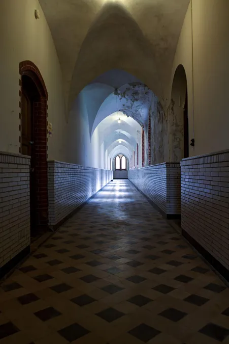 Donkere gewelfde gang met tegelvloer en licht aan het einde.