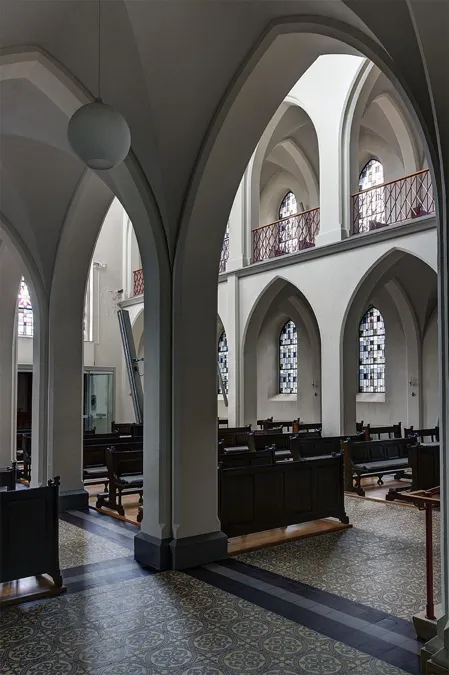 Doorkijk door een grote kapelboog naar banken en de hogere galerij.
