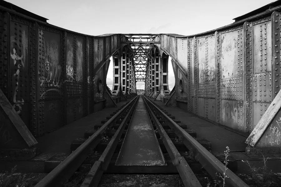 Symmetrisch zicht tussen hoge geklonken stalen wanden langs het spoor.