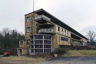 Edificio amarillo abandonado con una ampliación acristalada curva y balcones cubiertos.