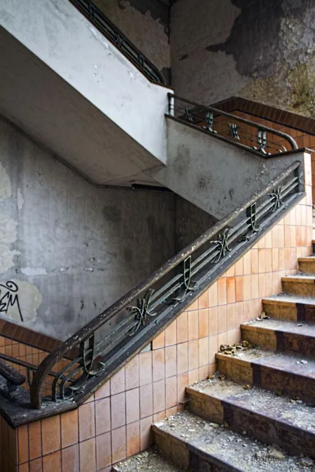 Geflieste Treppe mit Metallgeländer und abblätternden Wänden.