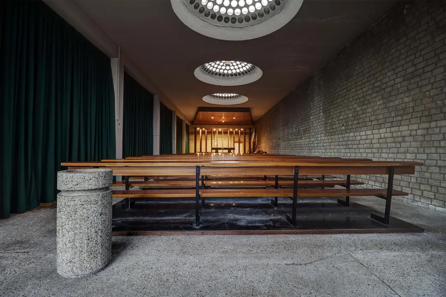 Long side chapel with round rooflights, green curtains and a granite holy-water basin in front.