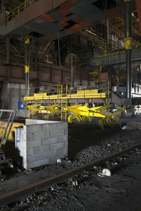 Yellow industrial lifting installation above rails in a dark hall.