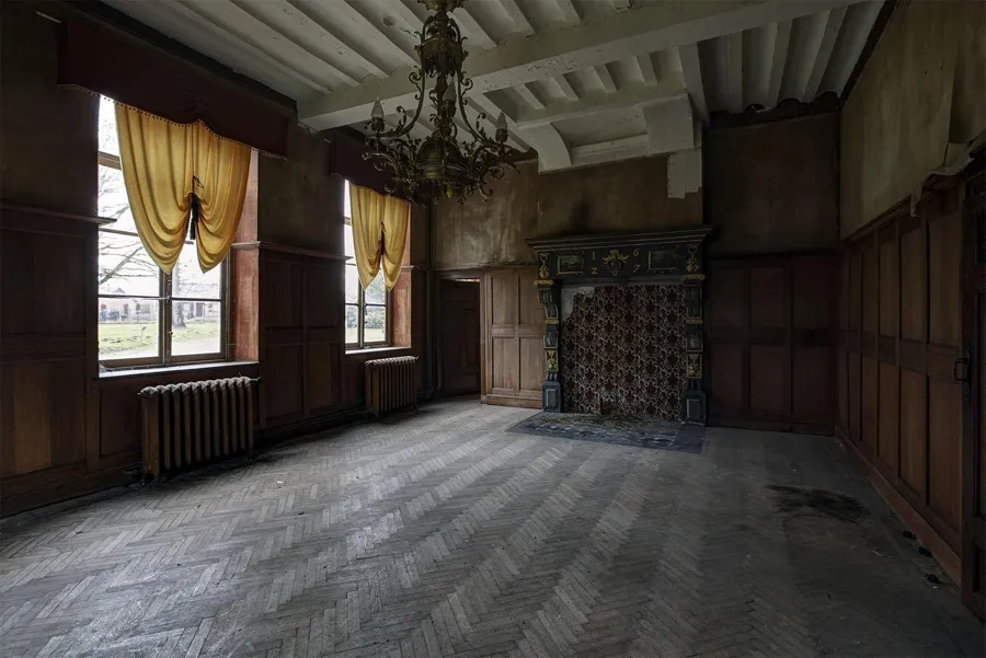 Salón vacío con revestimiento de madera, chimenea y lámpara de araña